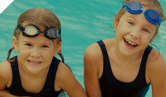 Girls in Pool Two young girls with swim goggles in the water near the edge of a pool